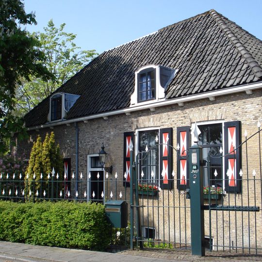 Boerderij, met dwars woonhuis onder hoog, pannen schilddak. Rechts een opkamer. Vensters met zesruitsschuiframen