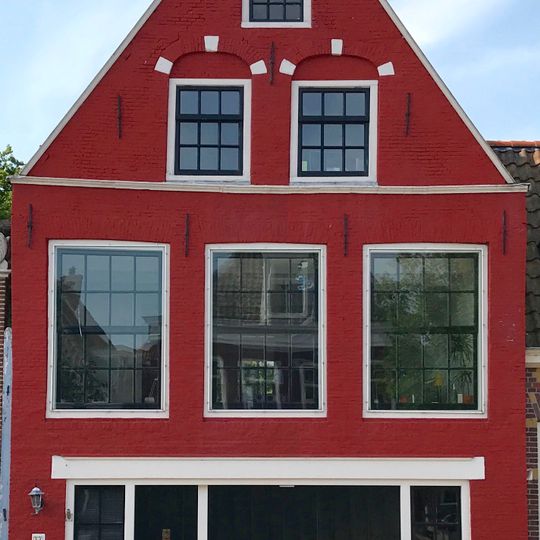 Pand onder zadeldak tegen puntgevel met waterlijst en in de top twee vensters onder geblokte bogen