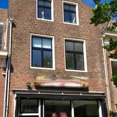 Hoog pand onder zadeldak tussen klokvormige voorgevel met aanzetkrullen en gezwenkte lijst en achtertopgevel