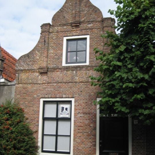 Huis. In- en uitgezwenkte topgevel met gemetselde pilasters. Pui gewijzigd