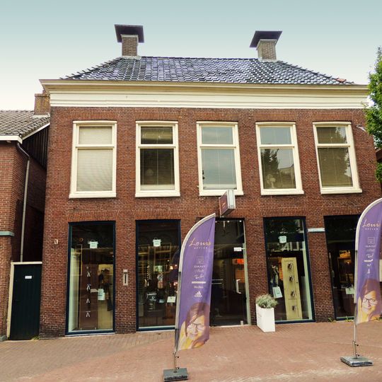 Vijf traveeën breed pand met verdieping en forse kroonlijst onder schilddak met twee hoekschoorstenen waarop borden