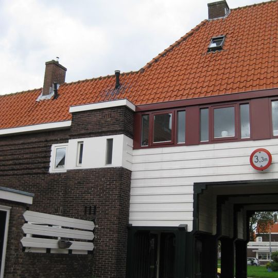 Poortgebouw met twee winkels met bovenwoningen, met veel hout zoals de zware kolommen in poort, bouwstijl Amsterdamse School, ligging aan Purmerweg centraal deel van Tuindorp Nieuwendam