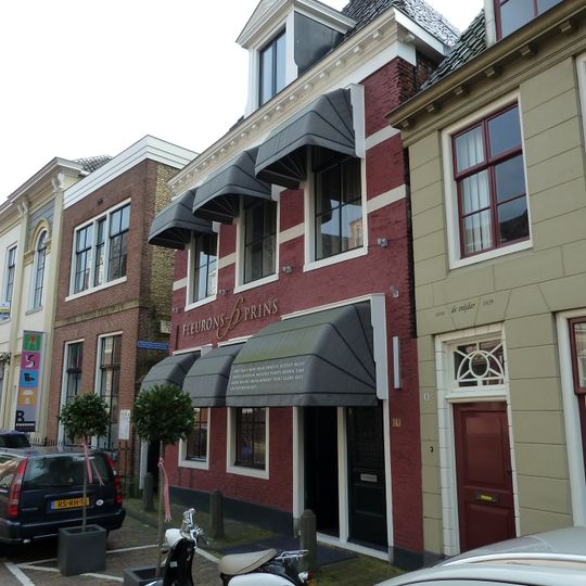 Pand met geblokte kroonlijst onder hoog zadeldak met aan voorzijde schild met dakkapel