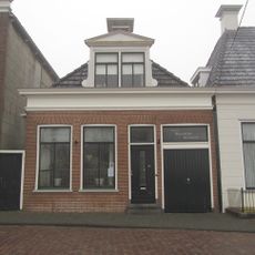 Laag pandje onder schilddak met grote dakkapel met classicistische details en topschoorsteen met bord