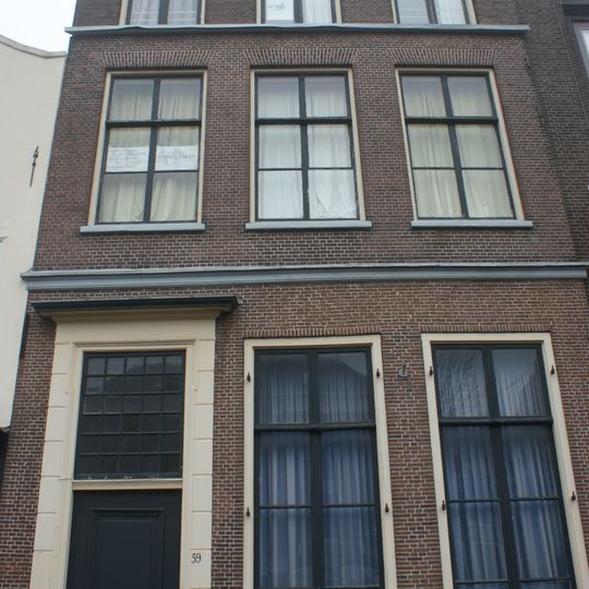 Pand met bakstenen gevel met rechte kroonlijst, later vernieuwde bovenbouw. Gesneden deur en omlijsting. Oorspronkelijke ruitverdeling en luiken aanwezig