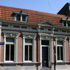 Woonhuis, gebouwd in het laatste kwart van de negentiende eeuw, in Eclectische stijl. Het hoekhuis heeft de voorgevel aan de Markt, de zijgevel grenst aan de Omgang.