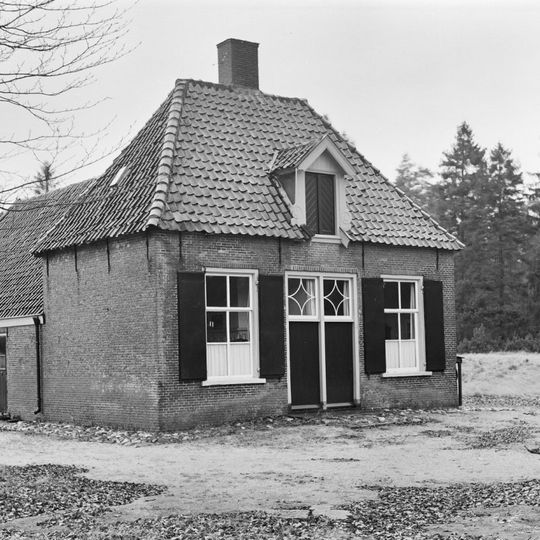 Kleine boerderij op T-vormige plattegrond. Woongedeelte onder pannen schilddak; dubbele deur met eenvoudige bovenlichten; vensters met luiken en zesruitsramen