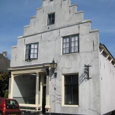 Gepleisterd pand met trapgevel, langgerekt zadeldak