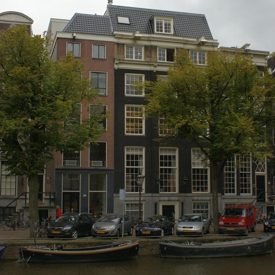 Pand met brede gevel van drie traveeën met middenrisaliet en hoeklisenen, onder rechte lijst met consoles