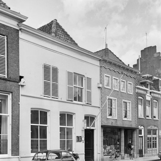 Pand met verdieping en schilddak, dat aan de achterzijde aansluit tegen een gepleisterde puntgevel. Voorgevel met kroonlijst