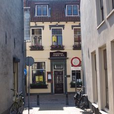 Gepleisterd eenvoudig woonhuis, grenzend aan de nauwe doorgang tot de mazijk