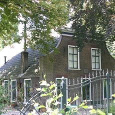 Boerderij met pannen wolfdak en voorgevel met houten kroonlijst en ingezwenkte zijkanten. Vensters met zesruitsschuiframen