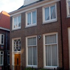 Eenvoudig pand, met rechte gootlijst en dakkapel. Stoep met eenvoudig hek