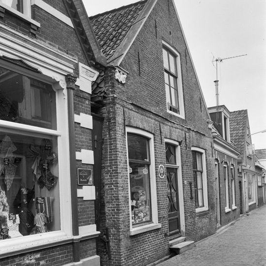 Pand onder zadeldak tegen puntgevel met vlechtingen langs de zijden en aanzetlijsten waaronder jaartalbinten