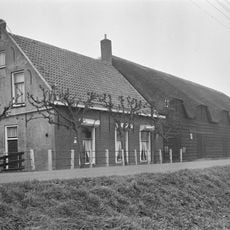 Boerderij met woonhuis onder pannen zadeldak met puntgevel. Grote, gepotdekselde schuur met rieten dak, dat boven de luiken vijf keer is opgewipt