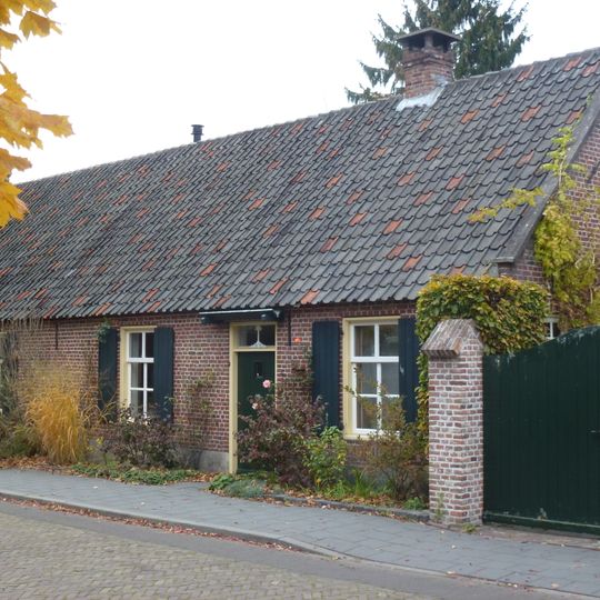 Landarbeiderswoning, bestaand uit twee evenwijdige vleugels onder zadeldaken met riet en pannen gedekt. Vensters met zesruitsschuiframen.