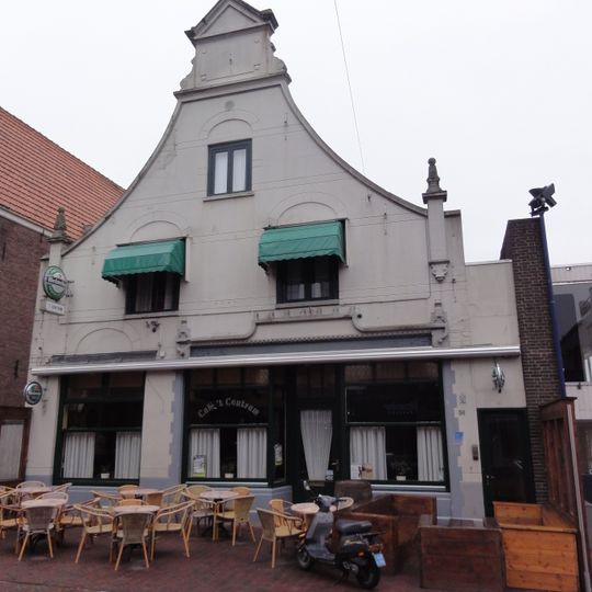 Huis onder zadeldak tussen achtertopgevel en in- en uitgezwenkte voorgevel, 18e eeuw, met 19e-eeuws pleister- en stucwerk.