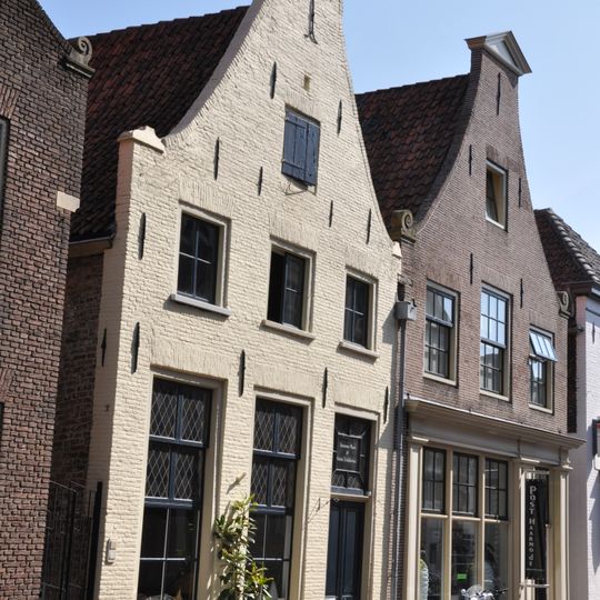 Pand met eenvoudige, gepleisterde klosgevel, met in de top een staafanker. Vrij goed bewaarde onderpui