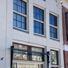 Pand onder zadeldak tegen gedrukte klokgevel met gebeeldhouwde aanzetkrullen, deklijst en bekroning