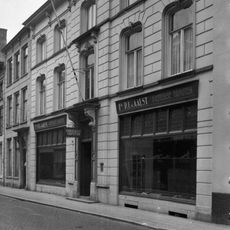 Huis met gebosseerd gepleisterde lijstgevel, waarin vensters met afgeronde bovenhoeken, kuiven van stuc en voluutvormige consoles onder de kroonlijst