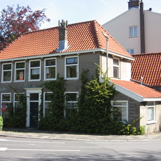 Op belangrijke hoekpunt gelegen rechthoekig, gepleisterd huis van parterre en verdieping met schilddak. Lijstgevel, waarin deur met eenvoudige pilasteromlijsting en hoofdgestel