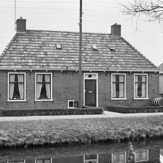 Dubbel landelijk pand met goot op klossen onder schilddak met twee hoekschoorstenen