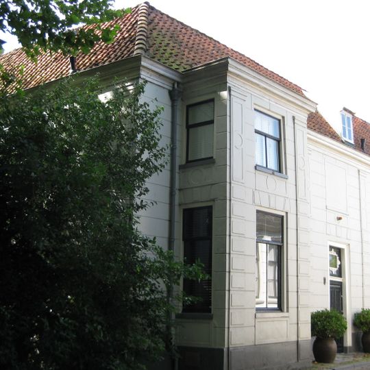 Huis onder schilddak met lijstgevel. Gebosseerde, witte voorgevel. Op verdieping twee gedichte vensternissen