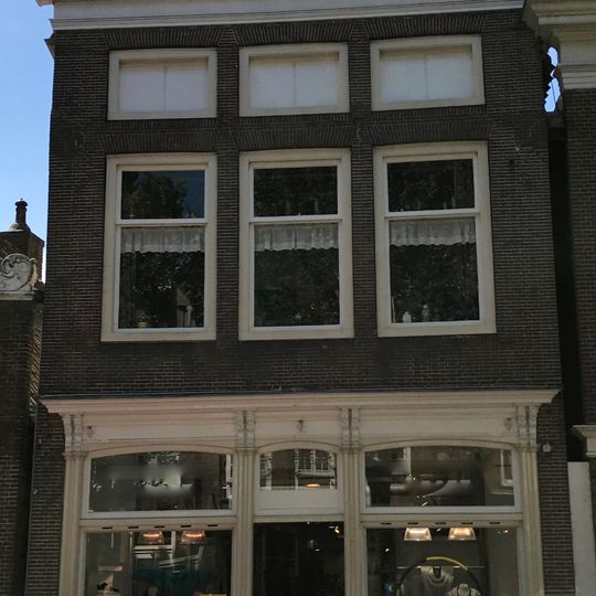 Hoog pand met vernieuwde voorgevel met lage vensters op zolderverdieping en kroonlijst onder zadeldak met voorschild waarboven topschoorsteen met bord