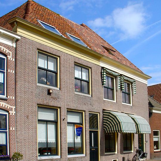 Pand bestaande uit twee huizen, waarvoor een voorhuis staat evenwijdig aan de straat en onder dwars schilddak