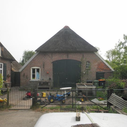 Schuur De Riete-Rietman, opgetrokken in rode machinale baksteen onder een deels met riet, deels met rode Hollandse pannen gedekt wolfsdak