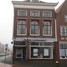 Hoekpand met lage zolderverdiepingvensters, rechte kroonlijst waarboven dakkapel en twee topschoorstenen