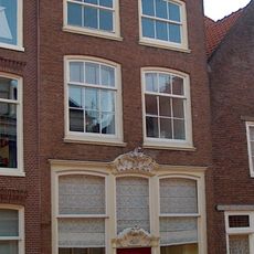 Huis met hoge bakstenen gevel met rechte kroonlijst waarop gesneden consoles en dakkapel, voor dwarskap. Venster met sterk gebogen strek en oude roeden.