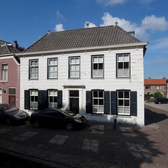 Hoekpand Lange Taam. Dwarshuis van parterre en verdieping onder zadeldak. Gepleisterde lijstgevels; aan de voorgevel gesneden bladconsoles in de lijst, Deuromlijsting met pilasters.