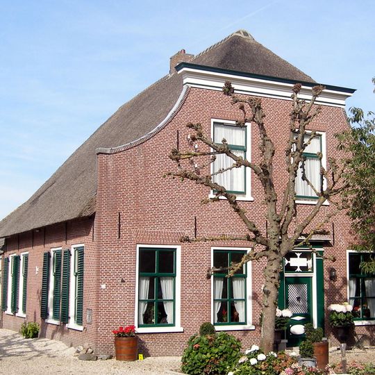 Boerderij. Voorgevel met ingezwenkte zijkanten en houten kroonlijst. Deuromlijsting met pilasters en hoofdgestel