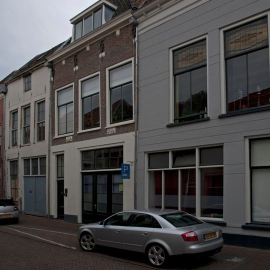 Pand met gepleisterde pui met boven de vensters van de verdieping restanten van ontlastingsbogen met muurankers