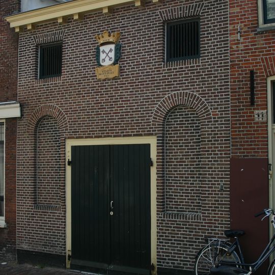 Pand met lage bakstenen gevel met houten goot. Blinde vensternissen, later verbrede pakhuisdeur waarboven gekroonde gevelsteen met opschrift "Stadts Brant Spueyten"