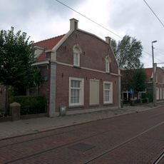 Dubbele rij van oorspronkelijk 24 rug-aan-rug gebouwde woningen op rechthoekige plattegrond, bestaande uit een bouwlaag onder met pannen gedekte mansardedak