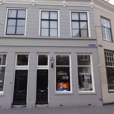 Huis met gebosseerd gepleisterde gevel met kroonlijst op consoles die voortzetting is van die van nr 66