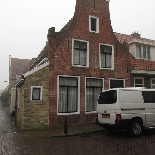 Pand met ongepleisterde gevel met aanzetkrullen onder zadeldak