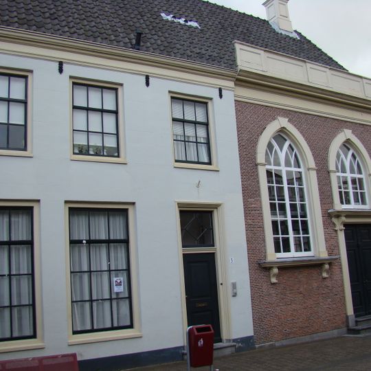 Pand met gepleisterde gevel met rechte kroonlijst, een geheel met kerkgebouw vormend