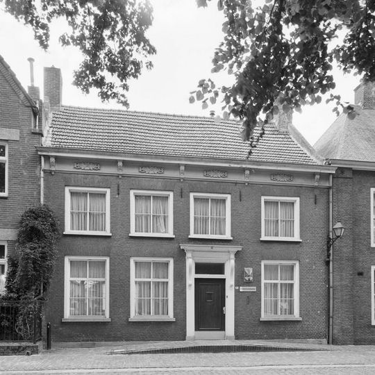 Huis onder dwars zadeldak en met lijstgevel; ingang met kroonlijst op voluutvormige consoles. Gootlijst op consoles