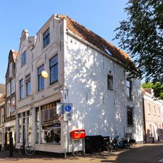 Pand met tot klokgevel gewijzigde gepleisterde trapgevel (top verdwenen) waarvan de dekplaten onder en boven bewaard zijn gebleven