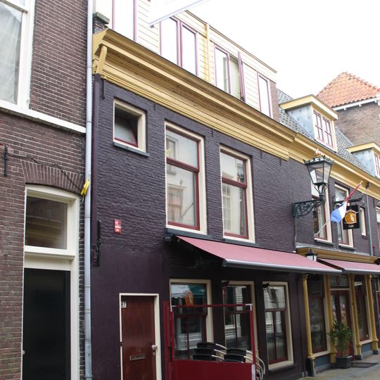 Pand met geverfde lijstgevel en jongere winkelpui onder dwars zadeldak en met restanten van de middeleeuwse stadsmuur