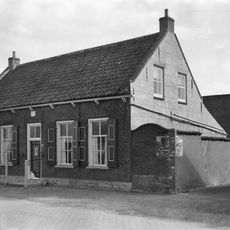 Huis onder zadeldak met langsgevel aan de Ring. Stoeppalen met krulijzers aan de gevel verbonden