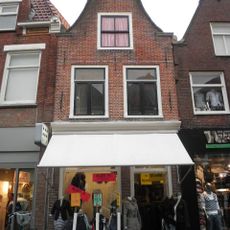 Smal pand waarvan de gevel door een ingezwenkte halstop wordt beëindigd met rococo kuifstuk