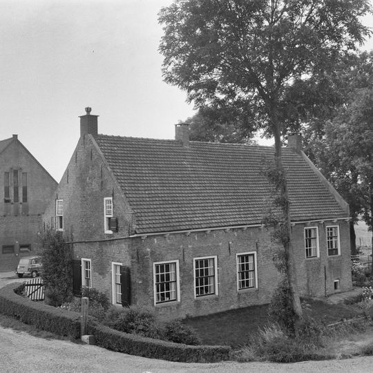 Boerderij waarvan alleen de afzonderlijke woning van belang is, met zadeldak tussen zijtopgevels, in de gevel nog sporen van de oorspronkelijke vensters met korfbogen waarin natuursteenblokjes