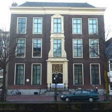 Pand met brede bakstenen gevel. Statig patriciershuis, rechte kroonlijst, gebeeldhouwde houten middenpartij in régence vorm. Hardstenen bordestrap met gesmeed ijzeren leuning