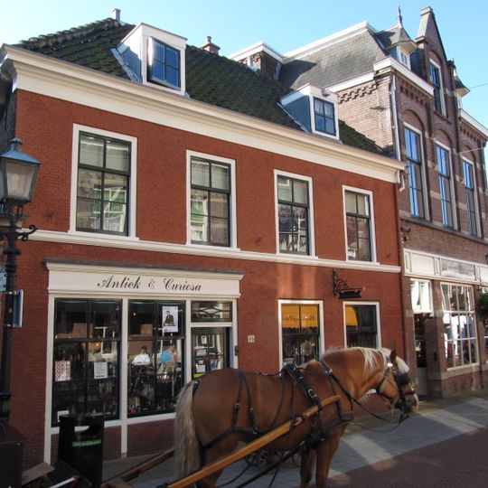 Pand met gevel met rechte kroonlijst, tegenover de kerk gelegen