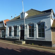 Huis met zadeldak, langsgevel evenwijdig aan de straat. Gepleisterde gevel. Aan de rechterzijde kelder. Stoep