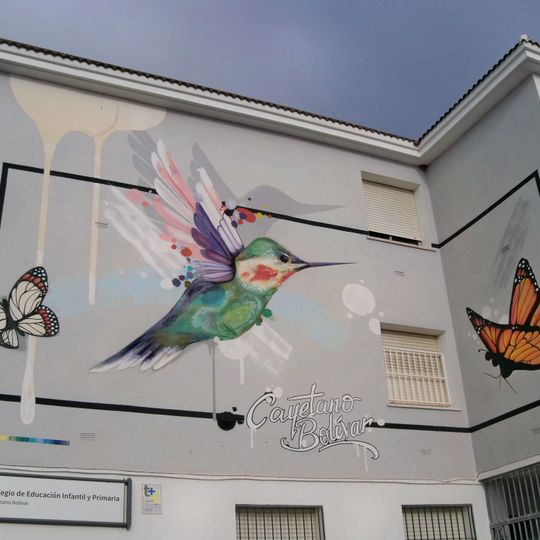 Mural con el nombre del colegio Cayetano Bolívar junto a la imagen de un colibrí y dos mariposas.